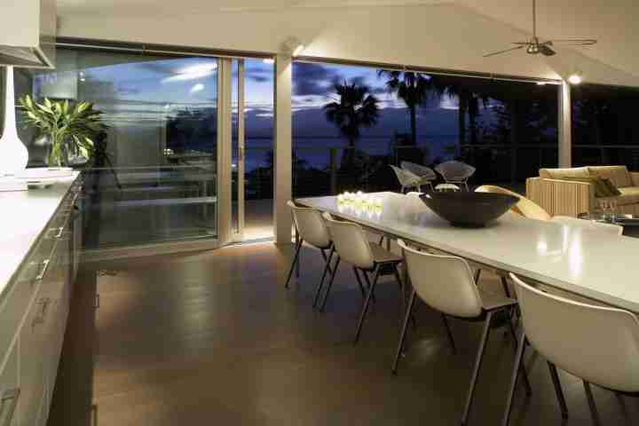 Large white dining table in modern open-plan kitchen with night time beach view